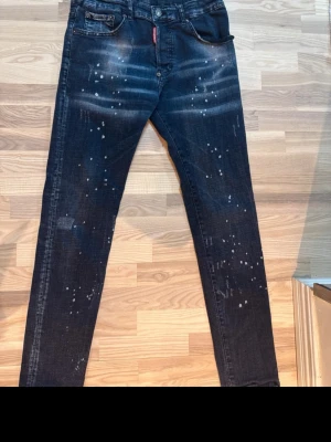 Dsquared2 jeans - Snygga mörkblå jeans från Dsquared2 med coola slitningar och vita färgstänk. Klassisk femficksmodell med röd logotagg vid gylfen. Jeansen har en smal passform och är tillverkade i bomullsdenim.