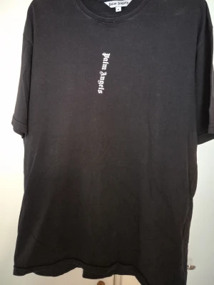 Svart Palm Angels t-shirt - Svart t-shirt från Palm Angels med vit logotyp tryckt vertikalt på både bröstet och ryggen. Oversized passform och klassisk rund halsringning. Perfekt för en streetwear-look.