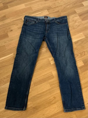 Mörkblå raka jeans från Boss - Snygga mörkblå jeans från Boss med klassisk rak passform. Jeansen har fem fickor, diskreta slitningar och kontrastsömmar. Perfekta för en avslappnad och stilren look. Tillverkade i denim med en autentisk känsla. Är i storlek 38 men på grund utav att det är slim så sitter de som en 36 nästan 34.
