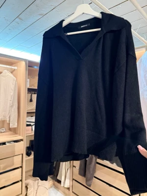 Svart stickad tröja med krage - Svart stickad tröja från Gina Tricot med avslappnad passform, djup v-ringning och bred ribbstickad kant vid ärmslut och nederkant. Tröjan har en snygg krage och är gjord i mjukt material, perfekt för lager-på-lager-stil.