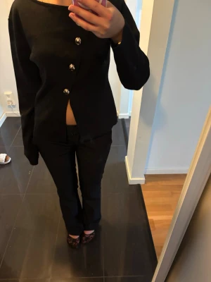 Svart blus med asymmetrisk knäppning - Trendig svart blus med lång ärm och fyra stora dekorativa knappar framtill.