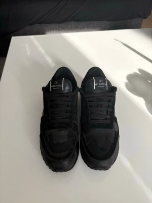 Svarta sneakers från Valentino - Snygga helsvarta sneakers från Valentino med klassisk siluett och diskret logga på plösen. Skorna har snörning och är tillverkade i en mix av mocka och syntetmaterial för en cool och stilren look.