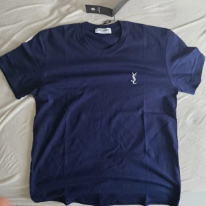 Marinblå t-shirt från Saint Laurent - Snygg marinblå t-shirt från Saint Laurent med klassisk rund hals och korta ärmar. Diskret YSL-logo broderad på bröstet. Perfekt för dig som gillar stilrena plagg med exklusiv känsla.