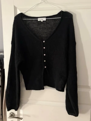 Svart tunn stickad tröja - Svart tunnstickad kofta från Gina med v-ringning. Lite ballongärm och lite croppad modell. Aldrig använd endast testad. Säljer för 230kr + frakt nypris 359kr🥰