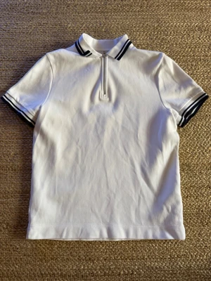 Vit piké med half zip och blå detaljer - Vit pikétröja med kort ärm och svart-randiga detaljer på ärmar och krage. Knappt använd.