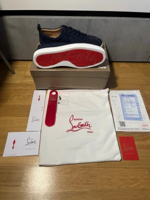 Mörkblåa loubs - Snygga marinblå sneakers från Christian Louboutin i mocka med ikoniska röda sulor och svarta nitar över hela tån. Lågt skaft och vita kanter på sulan ger en clean look. Kommer med originalpåse, skohorn och certifikat. Perfekta för dig som vill sticka ut.