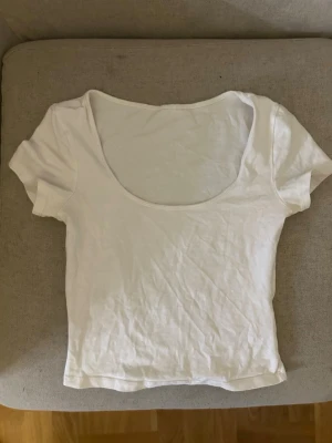 Vit croppad topp med rund hals - En enkel och stilren vit croppad topp med rund, djup halsringning och korta ärmar. Perfekt att matcha med jeans eller kjol för en avslappnad look. Materialet känns mjukt och lätt.