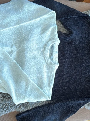 Stickade tröjor från H&M, vit och svart - Två stickade tröjor från H&M, en i krämvit och en i mörkgrått. Båda har rund halsringning och lång ärm. Materialet är mjukt och fluffigt, perfekt för att hålla sig varm. Enkel och stilren design som passar till jeans eller kjol.