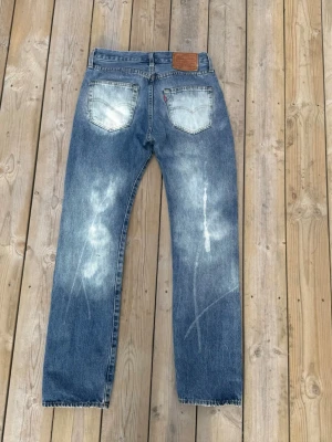 Levis 501 sällsynt design vintage - Säljer ett par klassiska blå Levi's jeans med raka ben och snyggt slitna detaljer på framsidan och baksidan. Jeansen har fem fickor, läderpatch bak och är gjorda i bomullsdenim. Perfekt för dig som gillar vintage och tidlös stil.