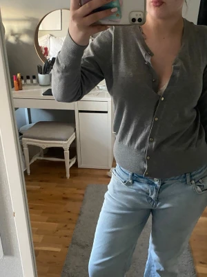 Grå basic kofta med knappar - En enkel och stilren grå kofta med rund halsringning och knäppning framtill. Koftan har långa ärmar och ribbade muddar vid ärmslut och nederkant. Perfekt att slänga över en topp eller bära som den är.