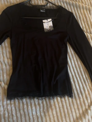 Lace detail scoop neck top - Svart långärmad topp från Ginatricot med snygg spetsdetalj vid halsringning och nederkant. Modellen har en fyrkantig hals och är figurnära, perfekt för att skapa en stilren look. Materialet är mjukt och stretchigt.