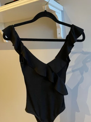 Svart body med volangdetaljer - Snygg svart body med djup urringning och volangdetaljer längs axelbanden och framtill. Använd fåtal gånger💕