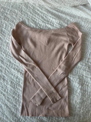 Ljusrosa ribbad offshoulder topp - Trendig ljusrosa ribbad topp med offshoulder-design och långärmade ärmar. Perfekt för att skapa en snygg och stilren look. Materialet är mjukt och stretchigt, vilket gör den bekväm att bära hela dagen.