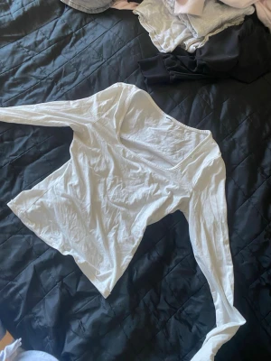Vit långärmad topp med v-ringning - Säljer en enkel och stilren vit långärmad topp med v-ringning. Perfekt att matcha med jeans eller kjol. Materialet känns mjukt och lätt, troligen bomull eller polyester. Passformen är normal och toppen är utan mönster eller extra detaljer.