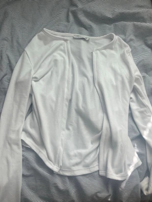 Vit långärmad kofta från 157 - En enkel och stilren vit långärmad kofta från 157 med öppen front och rund halsringning. Materialet är mjukt och stretchigt, perfekt att slänga på sig över en topp. Passar dig som gillar clean och minimalistisk stil.