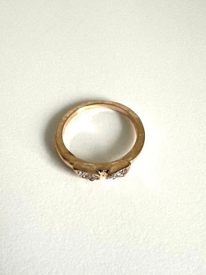 Guldfärgad ring med kristaller - Snygg guldfärgad ring med två bladformade detaljer som är dekorerade med gnistrande kristaller. Ringen har en stilren design som passar perfekt för att lyfta din look. Materialet är metall med syntetiska kristallstenar. 16mm inner-diameter. 