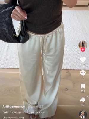 Krämvita satin byxor från Nelly storlek xs  - Snygga krämvita satinbhxor  med avslappnad passform och dragsko i midjan. Byxorna har en mjuk, flowy känsla och passar perfekt till en trendig vardagslook. Matcha med crop top eller stickad tröja för en chill stil.