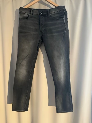 Svarta slim fit jeans från G-star - Snygga svarta slim fit jeans från G-star med tvättad och lätt sliten look. Klassisk modell med knappgylf och raka ben. Nästintill oanvända. Storlek W30 L32