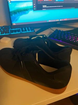 Svarta sneakers med brun sula - Säljer ett par stilrena svarta sneakers med klassisk design och brun gummisula. Skorna har snörning och är tillverkade i ett material som ser ut som läder. Perfekta för dig som vill ha en enkel och snygg look. Helt nya bara testade!!