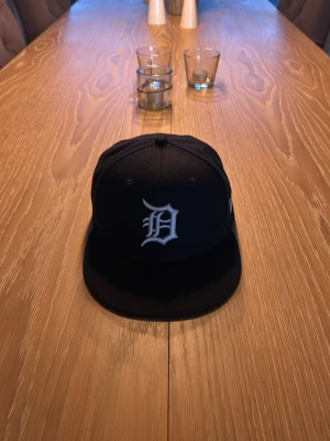 Svart New Era keps med D-logga - Säljer en svart keps från New Era. Klassisk snapback-modell med broderad New Era-logga på sidan. Perfekt för dig som vill ha en stilren och sportig look.                           storlek 60,6 cm