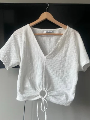 Vit topp med snörning från Zara - Säljer en vit topp från Zara med v-ringning och korta ärmar. Toppen har en ribbstickat tyg och snörning i midjan som ger en snygg detalj. Köpt secondhand för ett tag sen men har aldrig kommit till användning då jag tycker att den är lite för kort och liten på mig❣️