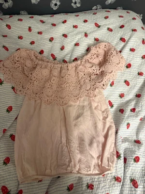 Ljusrosa offshoulder topp Colloseum - Supersöt ljusrosa offshoulder topp från Colloseum med bred virkad spets upptill. Toppen har en luftig passform och är perfekt för varma dagar. Materialet känns mjukt och toppen har en romantisk vibe med sin detaljerade spetskant.
