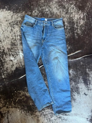Blå raka jeans med vintagekänsla Que sera sera - Säljer ett par klassiska blå jeans med rak passform och lätt slitna detaljer framtill och baktill. Jeansen har fem fickor och normal midja. Perfekta för en avslappnad och trendig look. 