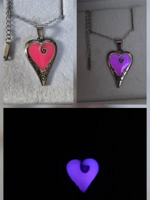 Glow in the dark hjärthalsband rosa/lila - Unikt handgjort halsband med ett hjärtformat hänge i silverfärgad metall och rosa emalj som lyser i mörkret med lila sken. Vanligt dagsljus utifrån och solljus aktiverar effekten så det sköter sig själv när du bär det som ett vanligt halsband. Lyser i flera timmar vid normal användning. Hänget har dekorativa snirkliga detaljer och spiral i mitten. Kedjan är tunn och justerbar i rostfritt stål. Perfekt för dig som gillar statement-smycken. Tål vatten & missfärgas ej, lång livslängd.