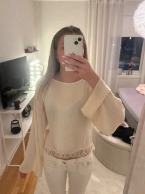 Champagne  topp med öppen rygg och spets - Snygg champagne topp med vida ärmar och spetsdetalj nedtill. Toppen har öppen rygg med omlottdetalj och knyt bak, vilket ger en unik look. Perfekt för dig som vill sticka ut lite extra. Materialet känns lätt och flowy.