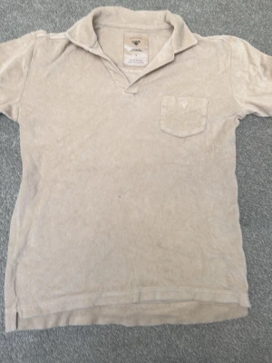 Beige frotté t-shirt med krage - Beige t-shirt från OAS i mjuk frotté med klassisk krage och bröstficka. Kortärmad modell med avslappnad passform, perfekt för en chill och stilren look.