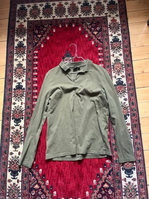 Olivgrön långärmad pikétröja - Olivgrön långärmad pikétröja med klassisk krage och knappar vid halsen. Tröjan är enkel och stilren,