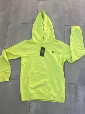 Neongul/lime färgad hoodie från Lyle & Scott - Cool neongul/limefärgad  hoodie från Lyle & Scott med klassisk huva och känguruficka. Märkets logga är broderad på bröstet. Perfekt för dig som vill sticka ut och gillar streetstyle. Stlk 164/170 rymlig! 