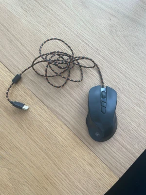 ADX Ultimate Gaming Mouse - Säljer en svart ADX Ultimate Gaming Mouse med USB-anslutning och flätad kabel i svart och orange. Musen har flera knappar för gaming.