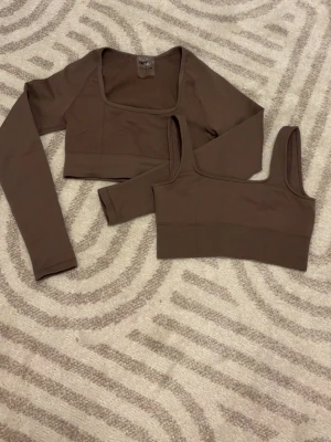 Brunt underklädesset med långärmad topp - Säljer ett brunt tränings sätt från Aim'n som består av en långärmad crop top med fyrkantig halsringning och en matchande sport-bh. Båda delar är tillverkade i ett mjukt och stretchigt material som sitter skönt mot kroppen. Perfekt för dig som gillar stilrena basics.