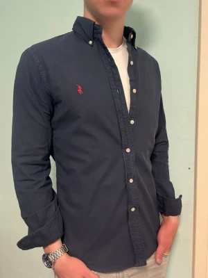 Marinblå Ralph Lauren skjorta – M Slim Fit - Säljer denna stilrena och snygga marinblåa Ralph Lauren skjorta. Skjortan är i mycket bra skick. Modellen är M slim fit.  Har du några frågor? Tveka inte att höra av dig. Allt gott från Deluxe garderoben ⭐️