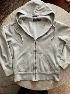 Grå zip hoodie från Polo Ralph Lauren - Snygg grå hoodie från Polo Ralph Lauren med dragkedja, huva och två stora fickor framtill. Såklart äkta ✅Klassisk blå logga broderad på bröstet. Säljer för att den har blivit för liten. Size s men passar xs också 👍. Om du har fråga hör av dig!