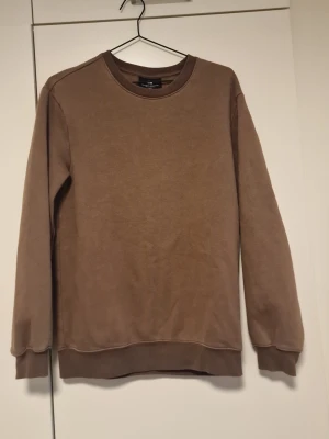 Brun sweatshirt från H&M - Enkel och stilren brun sweatshirt från H&M med rund halsringning och ribbade muddar vid ärmslut och nederkant. Tillverkad i mj sop bomullsblandning, perfekt för en avslappnad look. Passar lika bra till jeans som till mjukisbyxor.