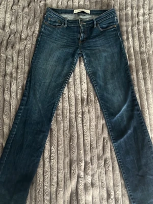 Mörkblå stretchjeans Abercrombie - Snygga mörkblå jeans från Abercrombie & Fitch med perfekt stretch. Klassisk femficksmodell och smal passform. Jeansen har subtila slitningar och kontrastsömmar för en trendig look. Perfekta till sneakers eller boots.