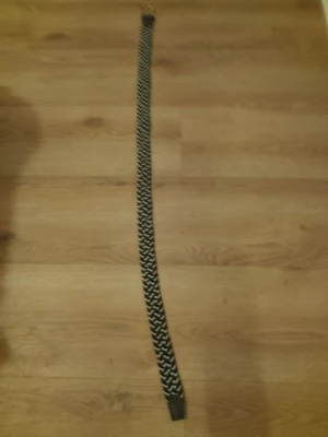 Svartvitt flätat bälte - Snyggt svartvitt flätat bälte med metallspänne och detaljer i skinnimitation. Bältet har ett randigt mönster och passar perfekt till jeans eller byxor för en stilren look. Kommer dock inte i orginal förpackning 