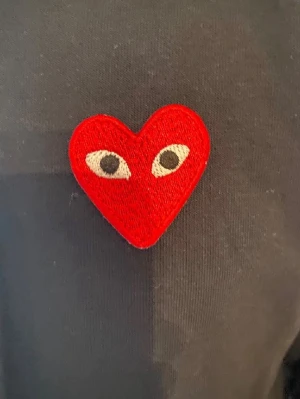 Svart hoodie Comme des Garçons Play - Svart hoodie med dragkedja från Comme des Garçons Play. På bröstet sitter det ikoniska röda hjärtat med ögon. Hoodien har fickor framtill och är tillverkad i mjukt bomullsmaterial. Perfekt för en avslappnad och trendig look.
