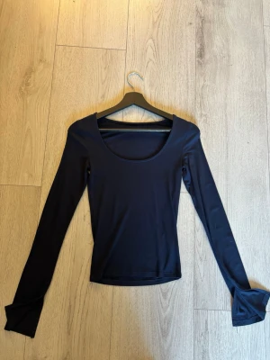 Mörkblå långärmad topp - En enkel och stilren mörkblå topp med lång snittad ärm och rundad halsringning. Tillverkad i ett mjukt och stretchigt material som sitter snyggt på kroppen. Perfekt att matcha med jeans eller kjol för en clean look.