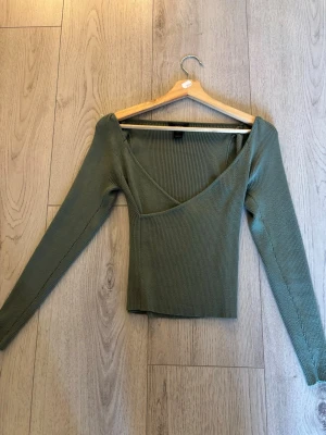 Grön ribbad topp från Lindex - Snygg grön ribbad topp från Lindex med v-ringad hals och lång ärm. Toppen har en croppad passform och är tillverkad i ett mjukt, stretchigt material som sitter skönt på kroppen. Perfekt att styla med höga jeans eller kjol.