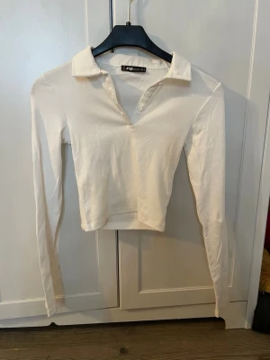 Vit ribbad långärmad polotopp - Säljer en vit ribbad långärmad polotopp. Toppen har en klassisk krage med knappar framtill och är croppad i modellen. Perfekt till jeans eller kjol för en clean och stilren look. Supersöt men tyvärr inte min smak då jag inte trivs i croppat. (Den är ändast lite kroppad). Pris kan diskuteras. Köparen står för frakt.