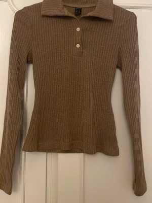Brun ribbad tröja från SHEIN - Säljer en brun ribbad långärmad tröja från SHEIN med krage och tre knappar framtill. Tröjan har figurnära passform och är tillverkad i ett mjukt, stretchigt material. Perfekt för dig som gillar en enkel men snygg stil.