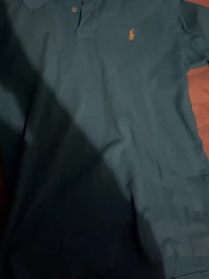 Blå pikétröja från Ralph Lauren - Klassisk blå pikétröja från Ralph Lauren med den ikoniska gula polospelaren broderad på bröstet. Tröjan har korta ärmar, krage och knappar vid halsen. Perfekt för en clean och stilren look. Helt ny utan prislapp och äkta. Skulle säga att det passar mest unisex S-M. Fast det står L. Fast passformen är unisex.