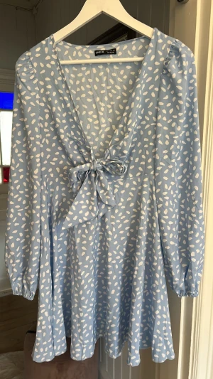 Ljusblå klänning  - Supersöt ljusblå klänning med vitt prickigt mönster. Klänningen har v-ringning, lång ärm och knytning framtill, aldrig använd!💕