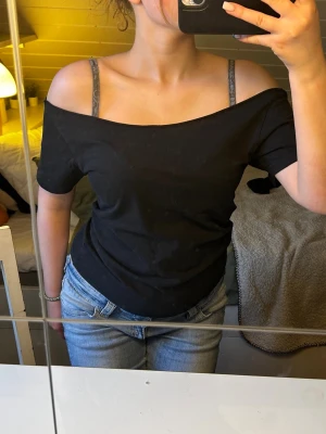 Svart offshoulder topp - Snygg svart offshoulder topp med korta ärmar och bred urringning som visar axlarna. Materialet är av mjuk bomull 100%. Har klippt off shoulder men den repar sig inte alls. 