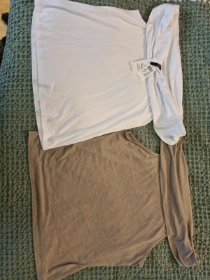 En vit och en beige offshoulder topp  - Säljer en vit och en beige/sandfärgad offshoulder topp med bred krage som kan bäras nedanför axlarna. Toppen är ärmlös och har en mjuk, känsla i ett tunt material. Perfekt för dig som gillar en enkel men trendig look.