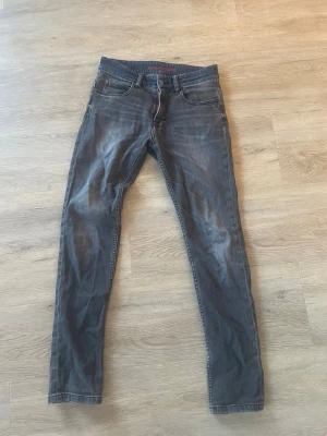 Gråa slim fit jeans från Zadig & Voltaire  - Säljer ett par mörkblå slim fit jeans från Zumo med klassisk femficksmodell och snygga slitningar. Jeansen har röda detaljer vid gylfen och är tillverkade i ett mjukt denimtyg som sitter tajt längs benen. Perfekta för en trendig och avslappnad look.