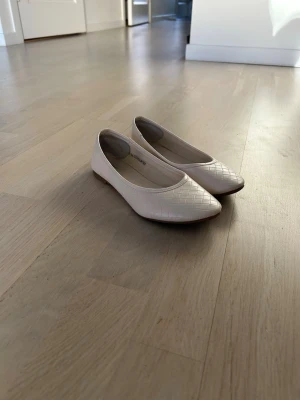 Vita ballerinaskor från XIT - Säljer ett par vita ballerinaskor från XIT med diskret flätmönster på ovandelen. Skorna har rundad tå och låg klack, material i syntet.